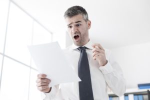 Businessman in the office receiving shocking bills and tax documents, he is gasping and screaming